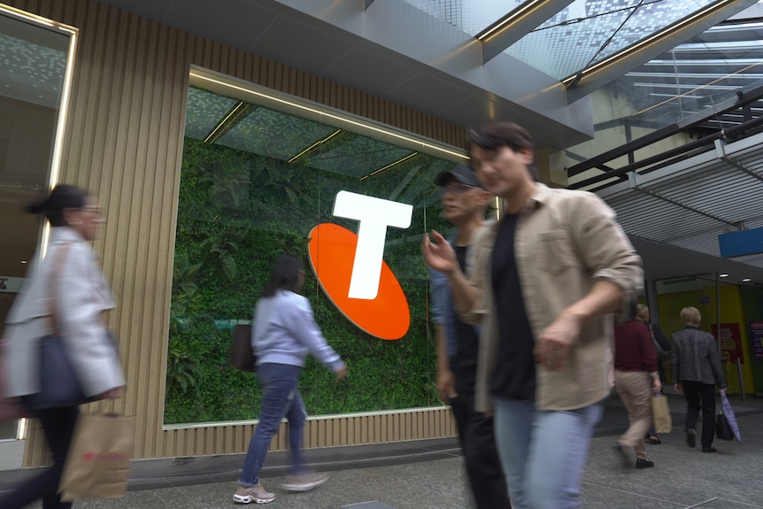 The orange and white telstra sign is in focus in the background as people walk past in a blur.