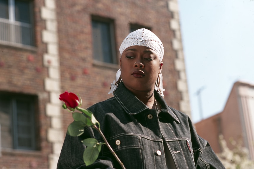 Da Brat with white bandana and nose ring looking sad holding a rose