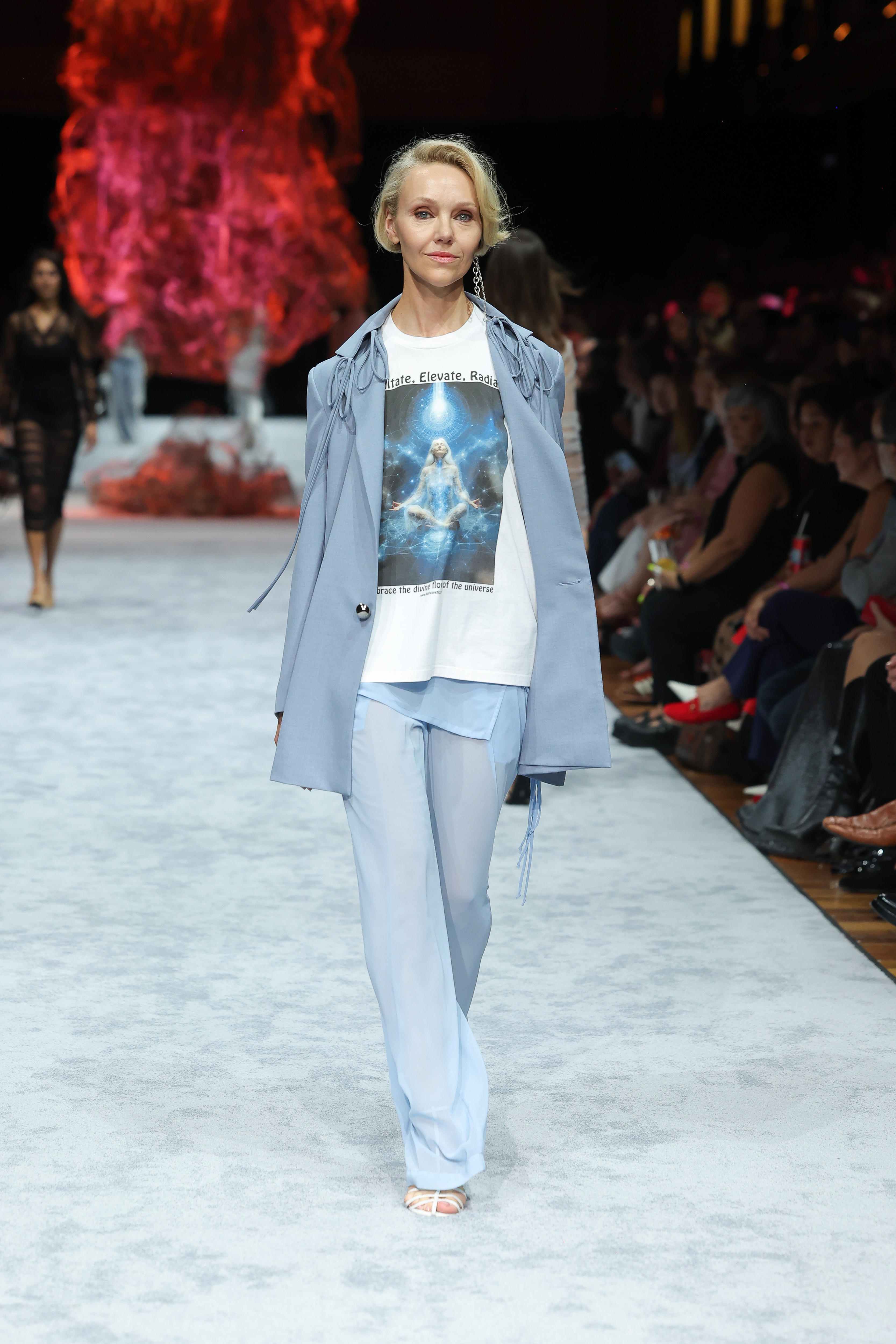 A model on a runway in a blue draped suit with a graphic T-shirt under the jacket.