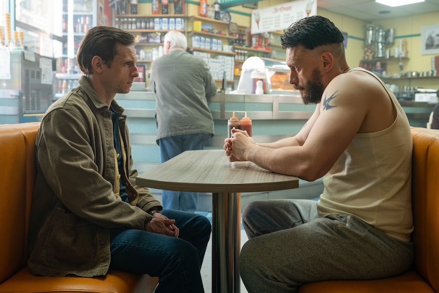 A TV still of Jamie Bell, 40, sitting across a table in a diner from a beefed-up Richard Gadd, 37, in a singlet, looking severe.