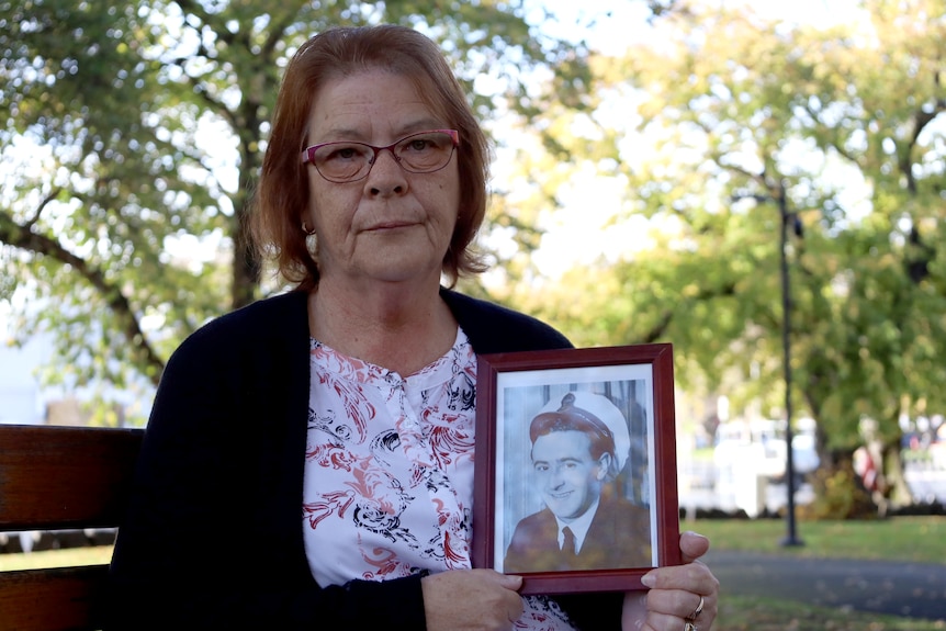 A woman with red hair holds an old photo of her father.