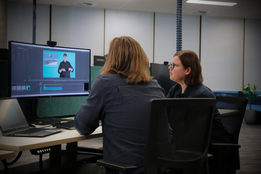 Two women sitting at a computer editing a video. 