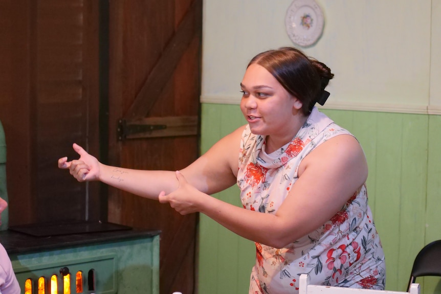 Woman in floral dress makes gesture.