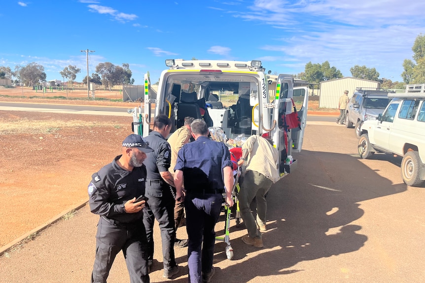A group of people putting a man on a stretcher into an ambulance.