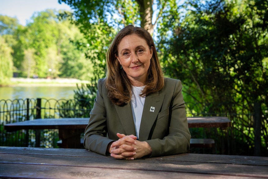 A woman sitting on an outdoor table smiles at the camera.