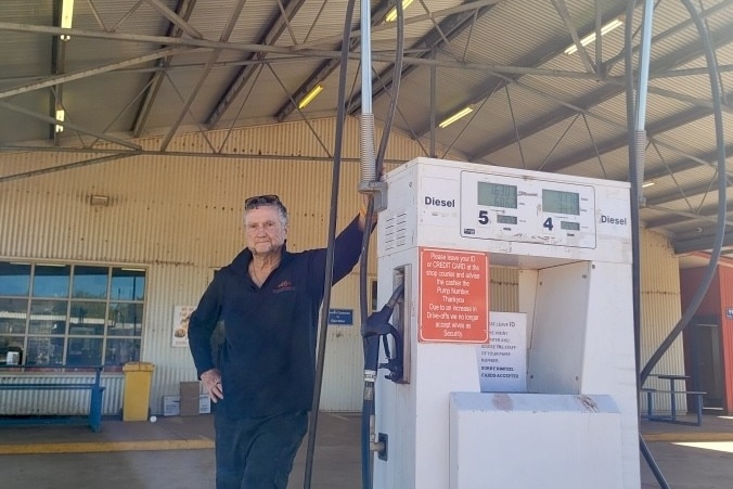 man with grey hair and blue shirt standing next to a fuel pump 