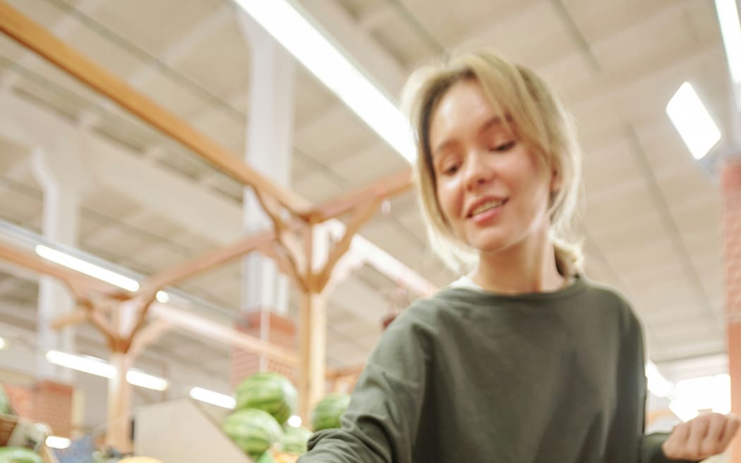 A woman reaches to grab a tomato from the grocery section in a supermarket.