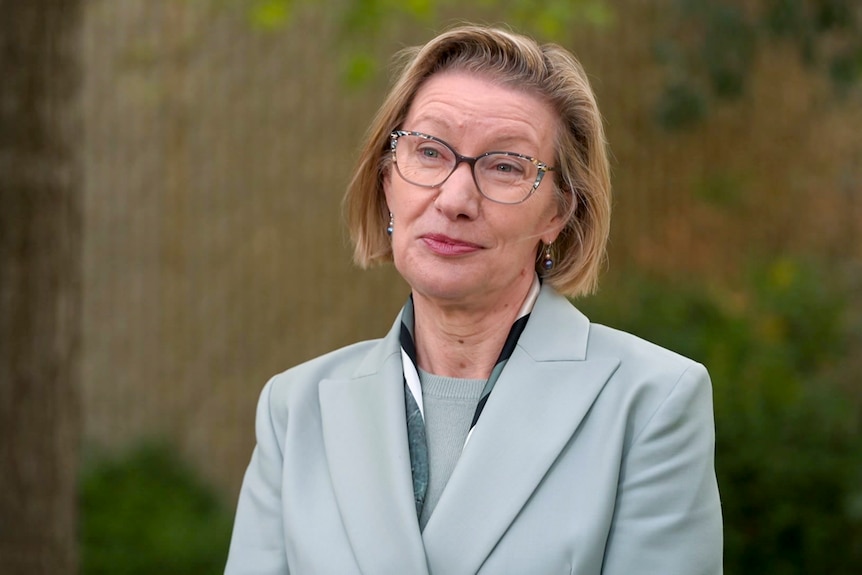 A woman wearing glasses and a grey suit jacket.