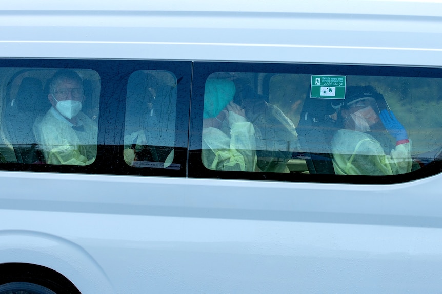 A group of people in full body protective gear are in a minibus