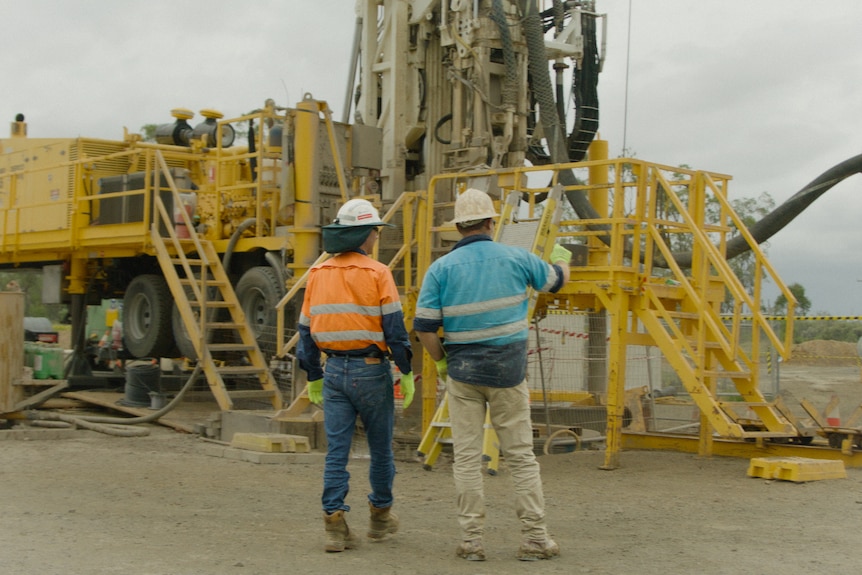 Two men in hi-vis jackets stand in front of railing and stairs near a mining shaft.