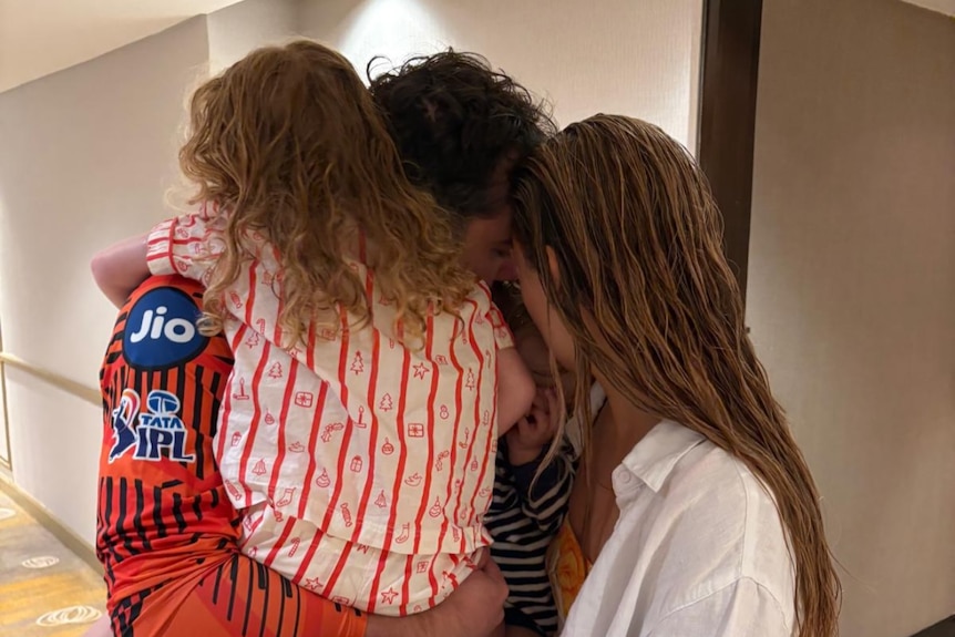 A woman and a girl hugging a man in a corridor