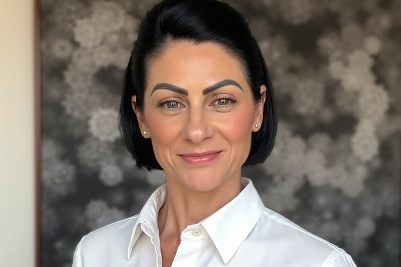 A woman with black hair wearing a white blouse smiling into the camera.