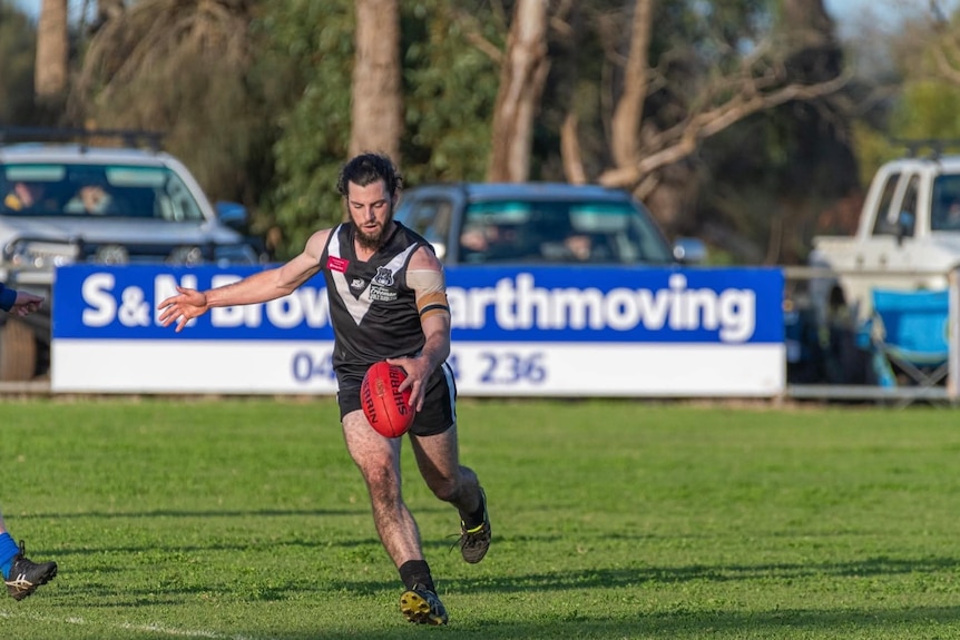 A man in a black and white footy uniform goes to kick a drop punt.