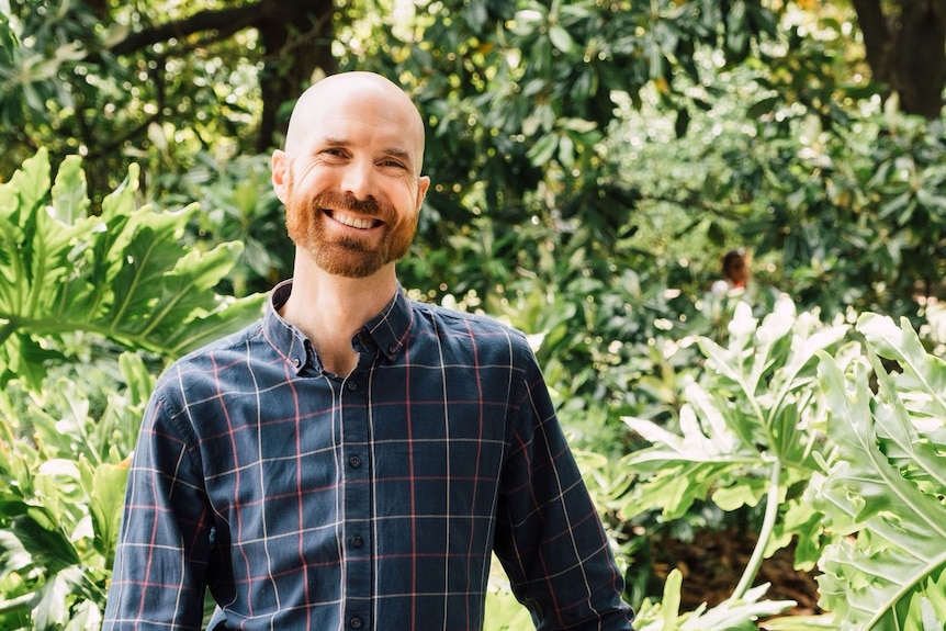 A man in long-sleeve shirt in front of a green backdrop.