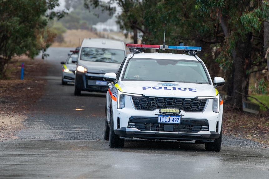 a police car drives ahead of a white minibus on a road