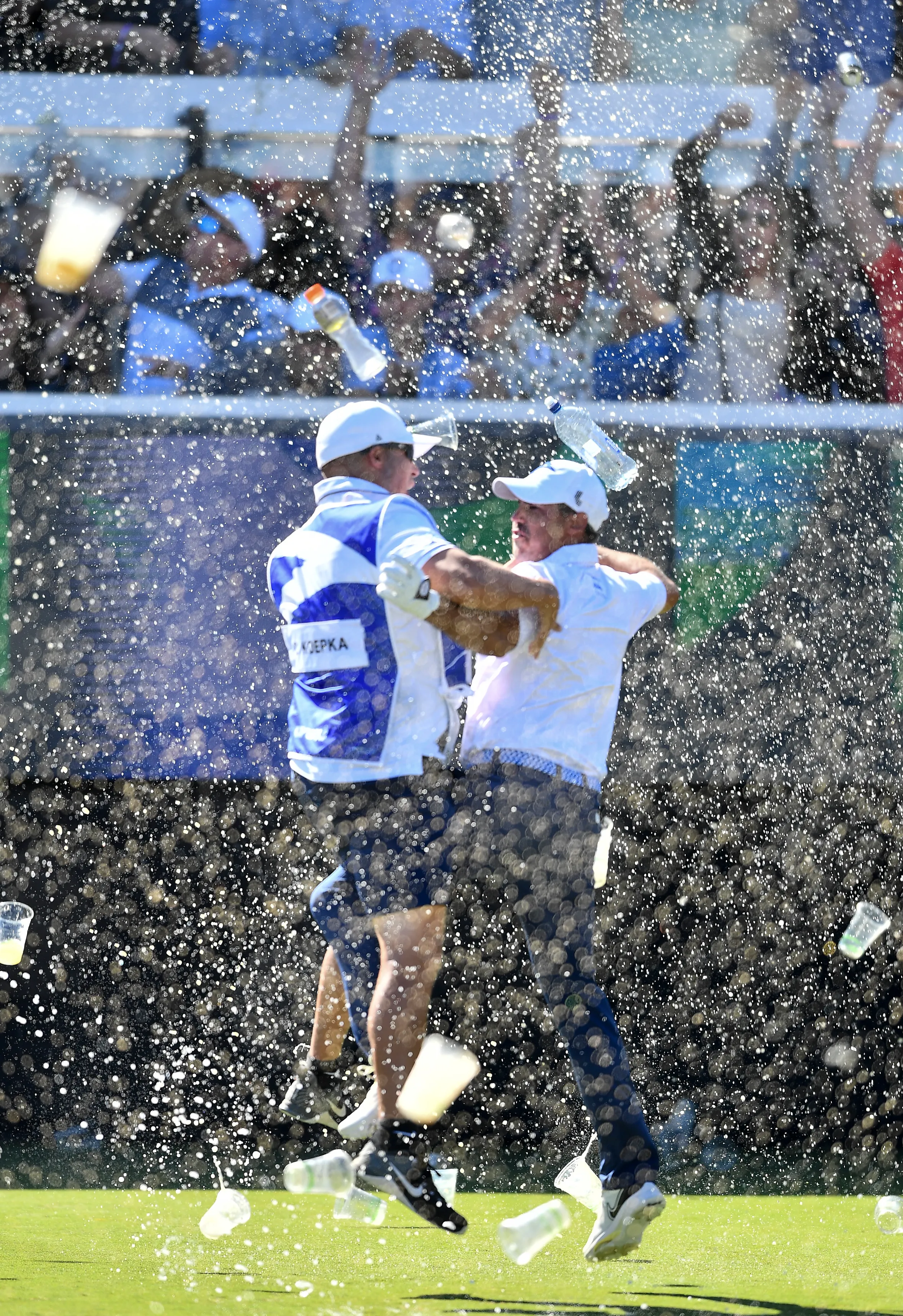 Chase Koepka celebrates a hole-in-one with his caddie, being showered in beer from the crowd.