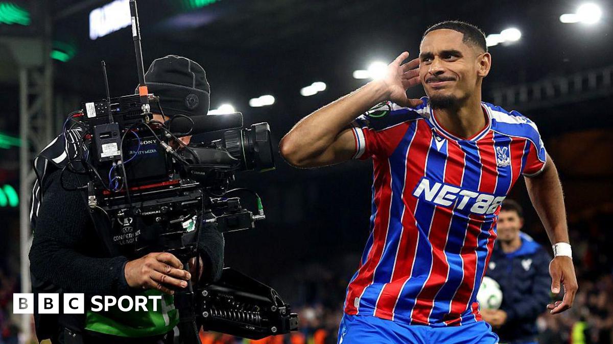 Crystal Palace's Maxence Lacroix cups his right ear with his right hand as he stands next to a TV camera