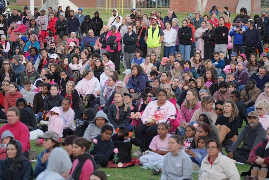Big numbers at a vigil, people sitting on the grass.