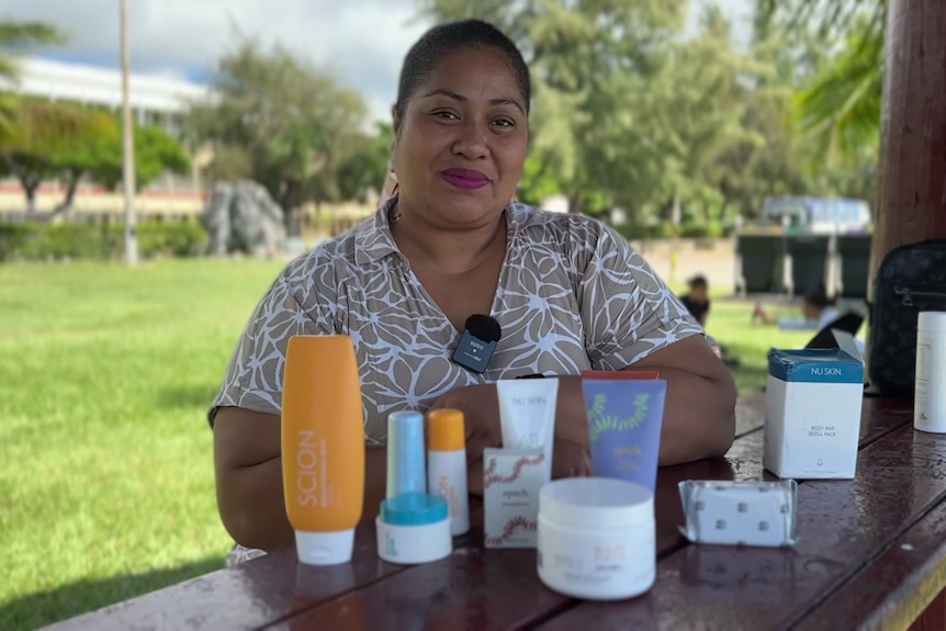 A woman sits at a bench with beauty products in front of her smiling