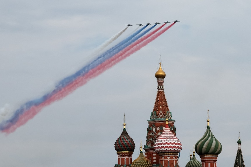 The turrets of an iconic Russian building, wiht several planes flying overhead leaving a trail of colourful smoke.