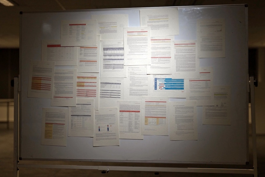 A whiteboard in an office covered in dozens of pages of paper that appear to be from reports or other documents.