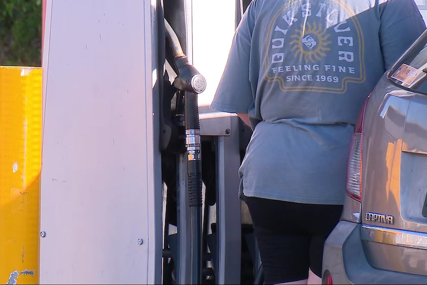 A close-up shot of a person's back as they stand at a petrol bowser filling up their car.
