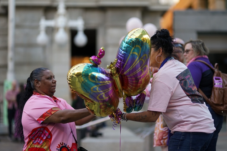 Two Indigenous women holding buttefly balloons at a vigil.