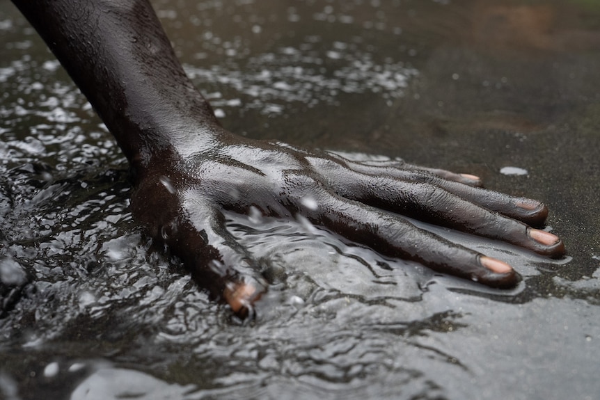 A photo of a man's bare hand in muddy waters.