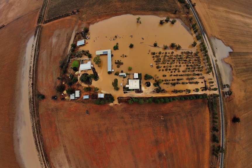 A birds eye view of brown land flooded with brown water, pooling around buildings and trees.