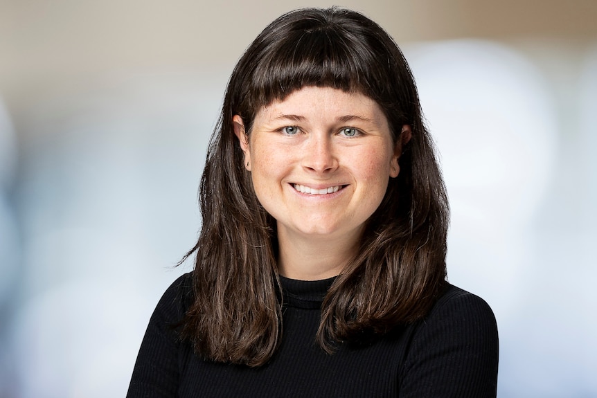 A woman in a black long-sleeved top with dark hair and crossed arms smiles at the camera