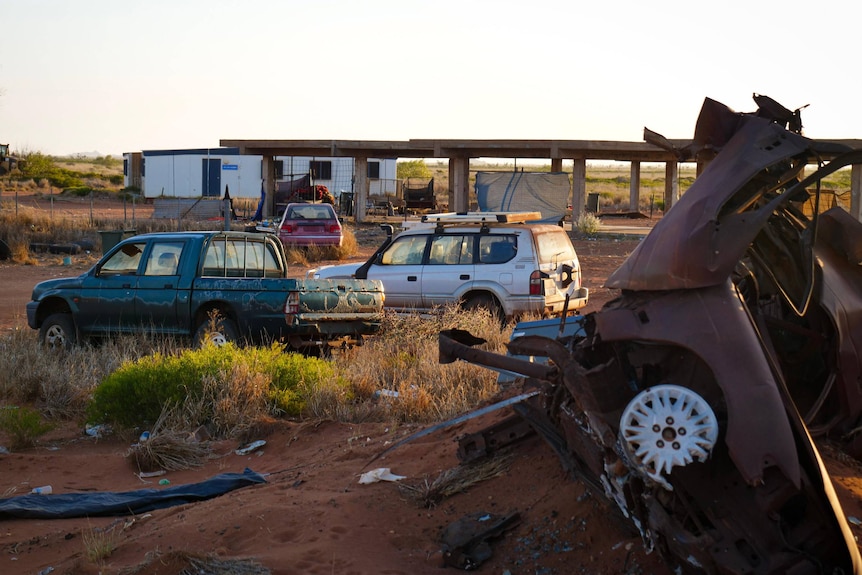 Abandoned husks of cars litter a desert patch of red dirt.