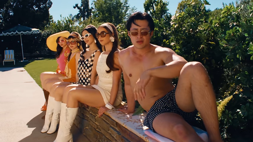 A scene from Laufey's Madwoman music video, including Hudson Williams and other women sitting by the pool.