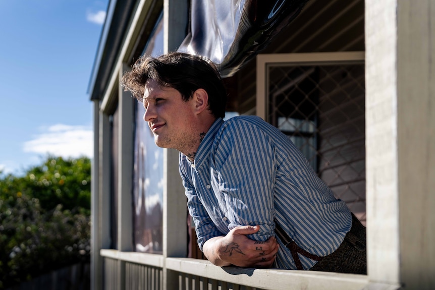 A man with tattoos looks out to the distance on a balcony