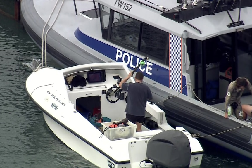 A man holds a spearfishing gun as he stands on a small white boat