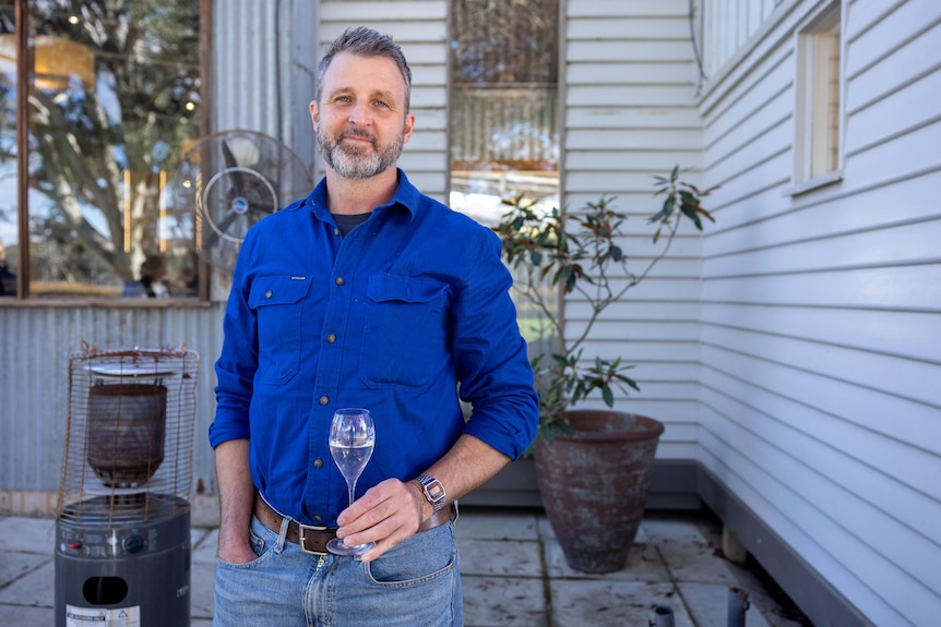 A man in a blue shirt hold a glass of wine 