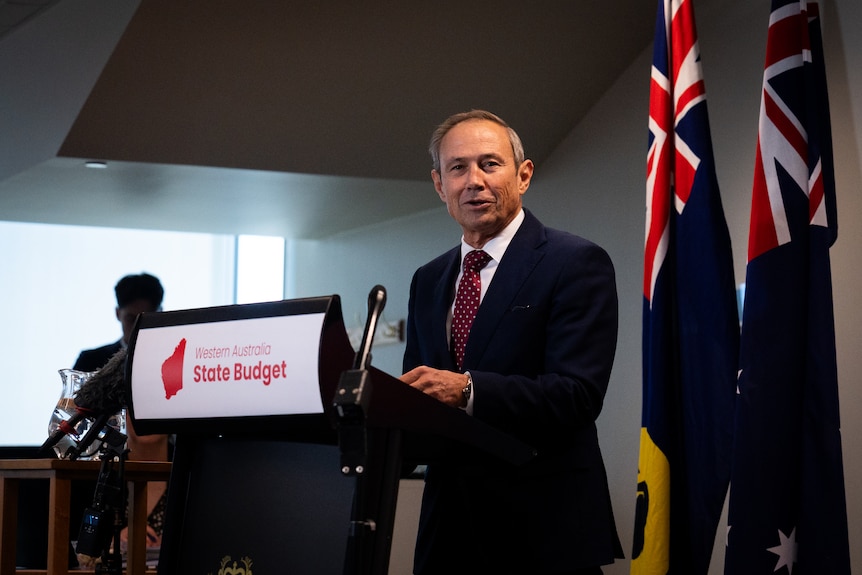 Roger Cook smiles for the camera as he stands at a lecturn
