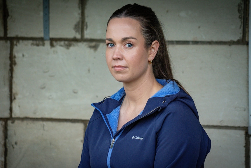 A woman wearing a dark blue jacket with brown hair and blue eyes looks at the camera.