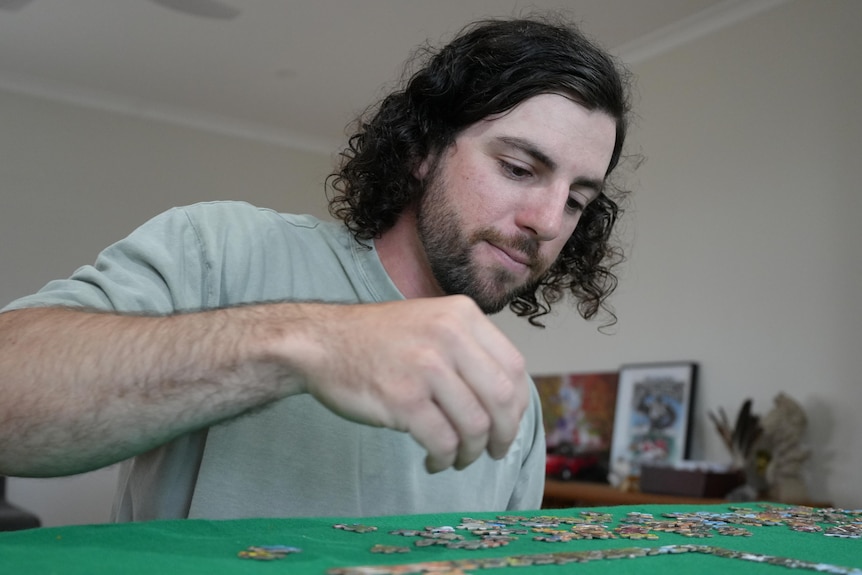 A man holds a puzzle piece and attempts to solve a large puzzle.