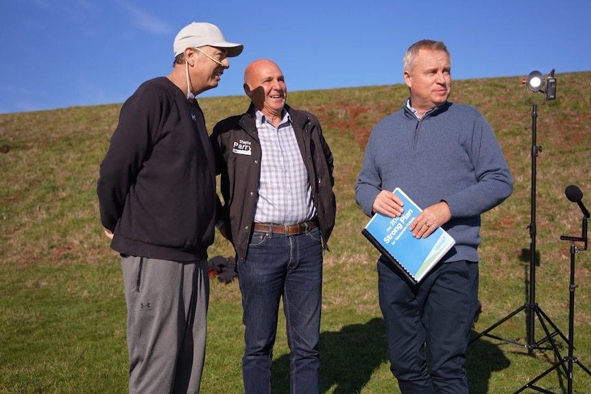 Three men stand on a hill, looking off into the distance.