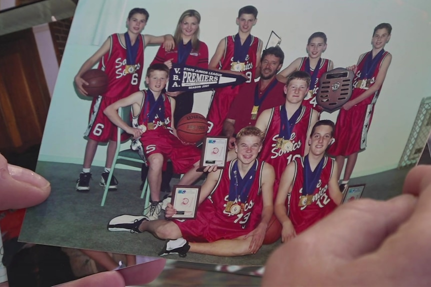 A person's hands holding a photograph of a team of boys in basketball gear.