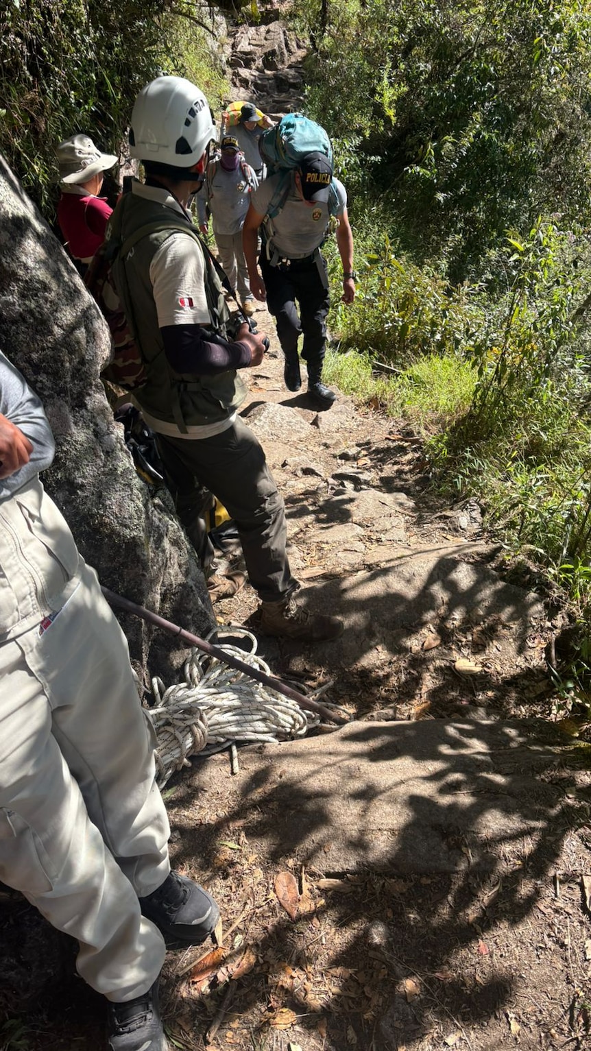 Men wearing protective helmets standing along a thin, uneven jungle hike trail.