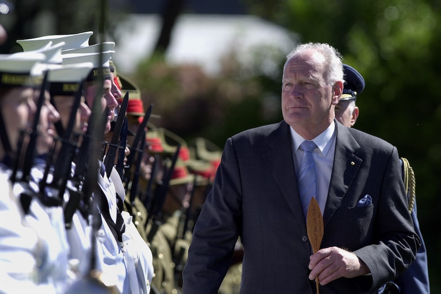 Peter Hollingworth walks alongside a row of military personell standing at attention, all hold rifles