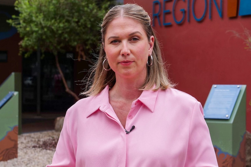 A blonde woman in a blouse stands near a municipal building.