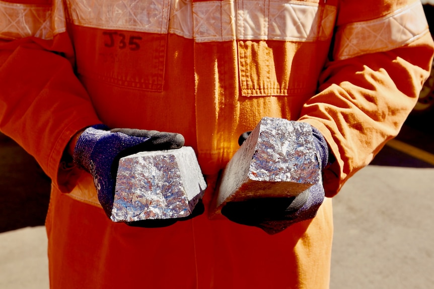 A man in an orange uniform holding an antimony ingot in his hands.