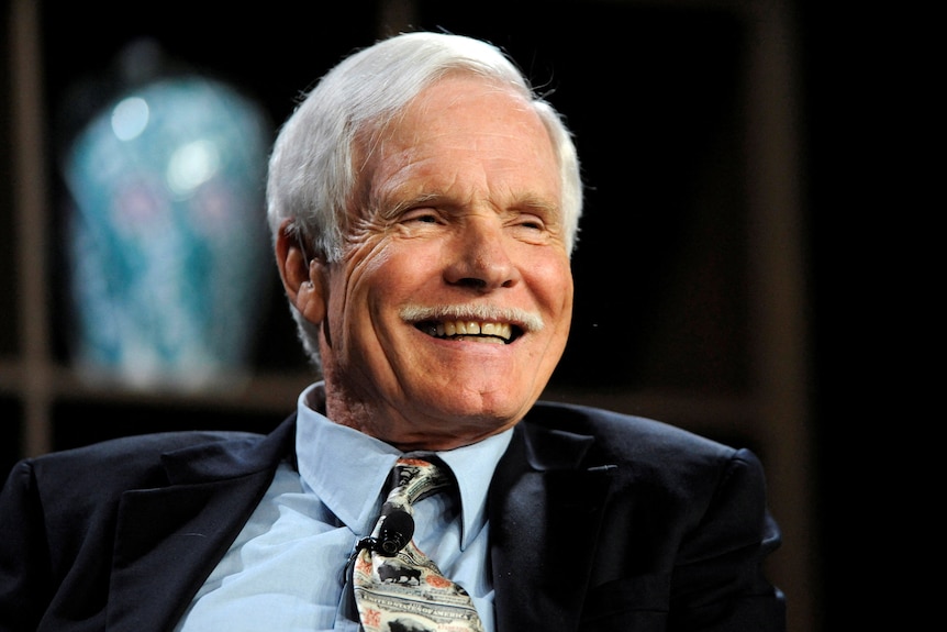 Turner, wearing a tie with a dollar bill pattern, smiles.