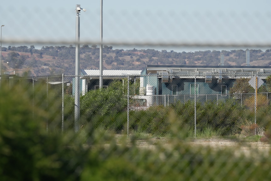 The exterior of a beige coloured building behind a fence