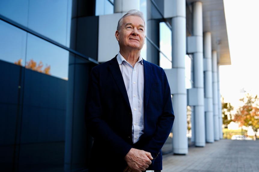 A man in a suit stands infront of a building looking away from the camera