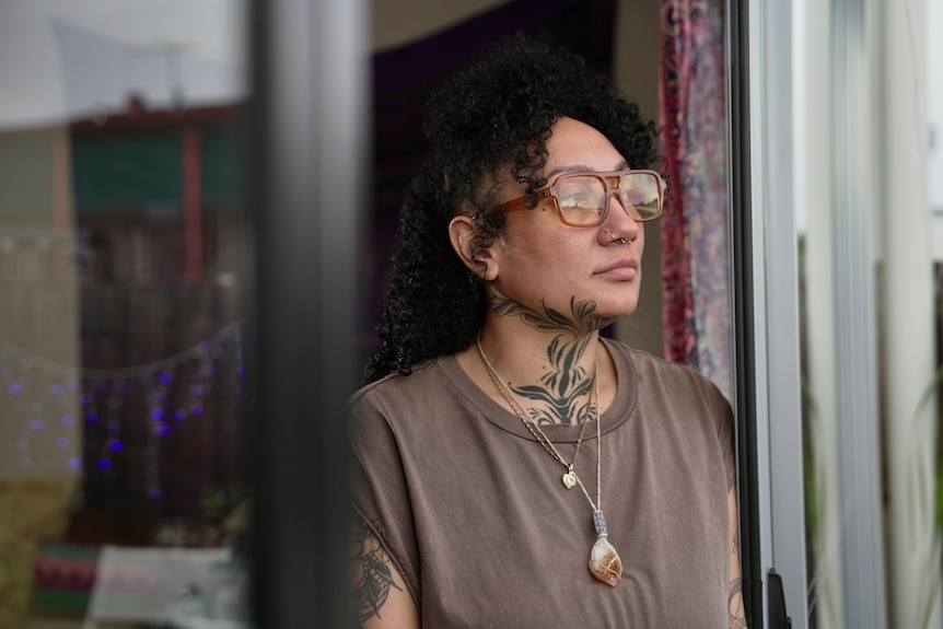 Woman with black curly hard and yellow glasses looking out a window frame