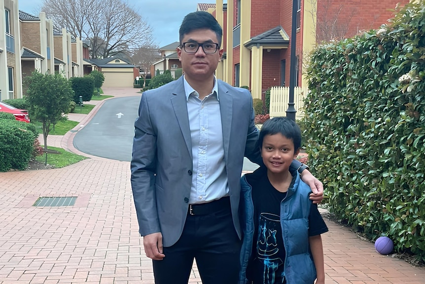 Picture of a man standing with his son and they are both smiling to the camera.