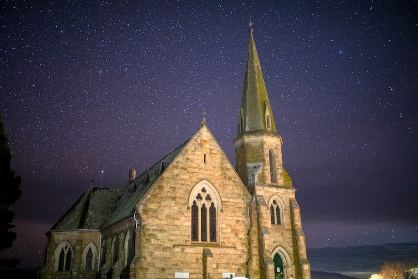 A long exposure of starry sky scene above cream brick church with steeple.